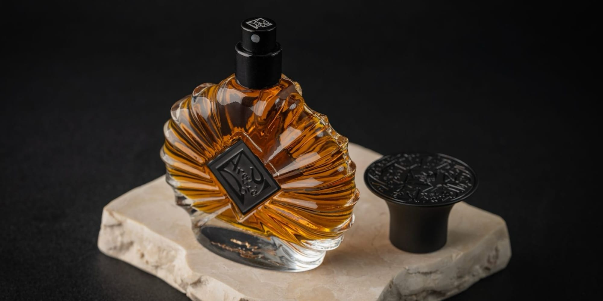 Amber perfume bottle on raw travertine stone, lit against near-black